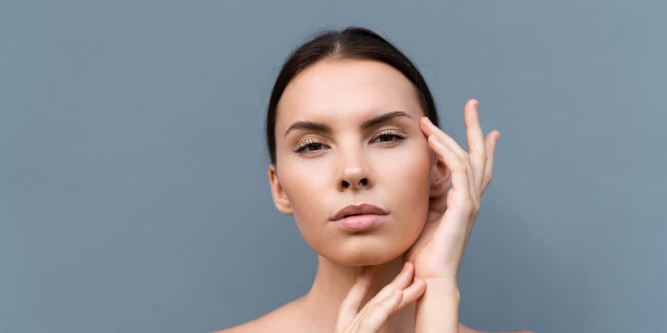 close up beauty portrait of a topless woman with perfect skin and natural make up on light blue wall background