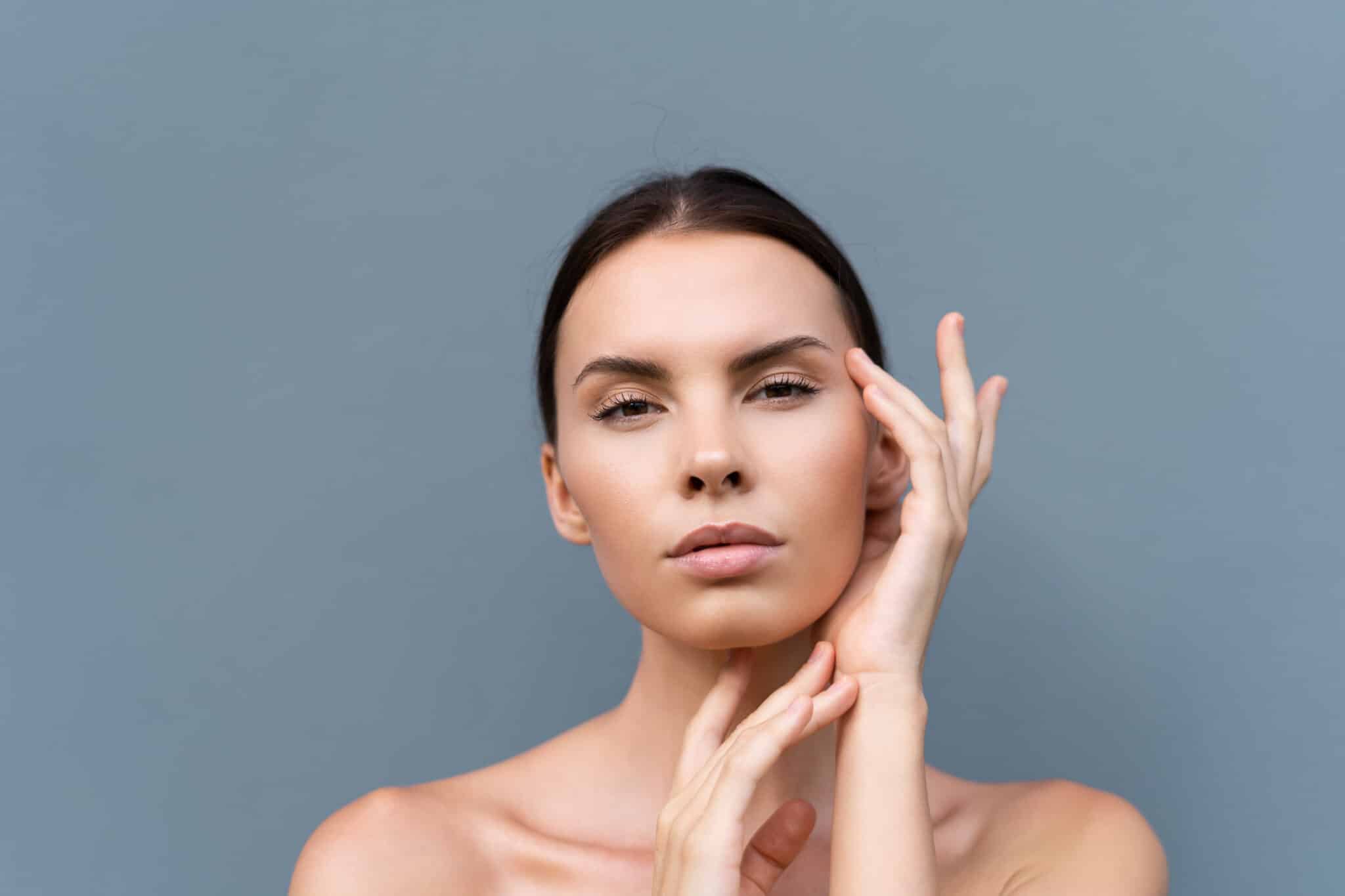 close up beauty portrait of a topless woman with perfect skin and natural make up on light blue wall background